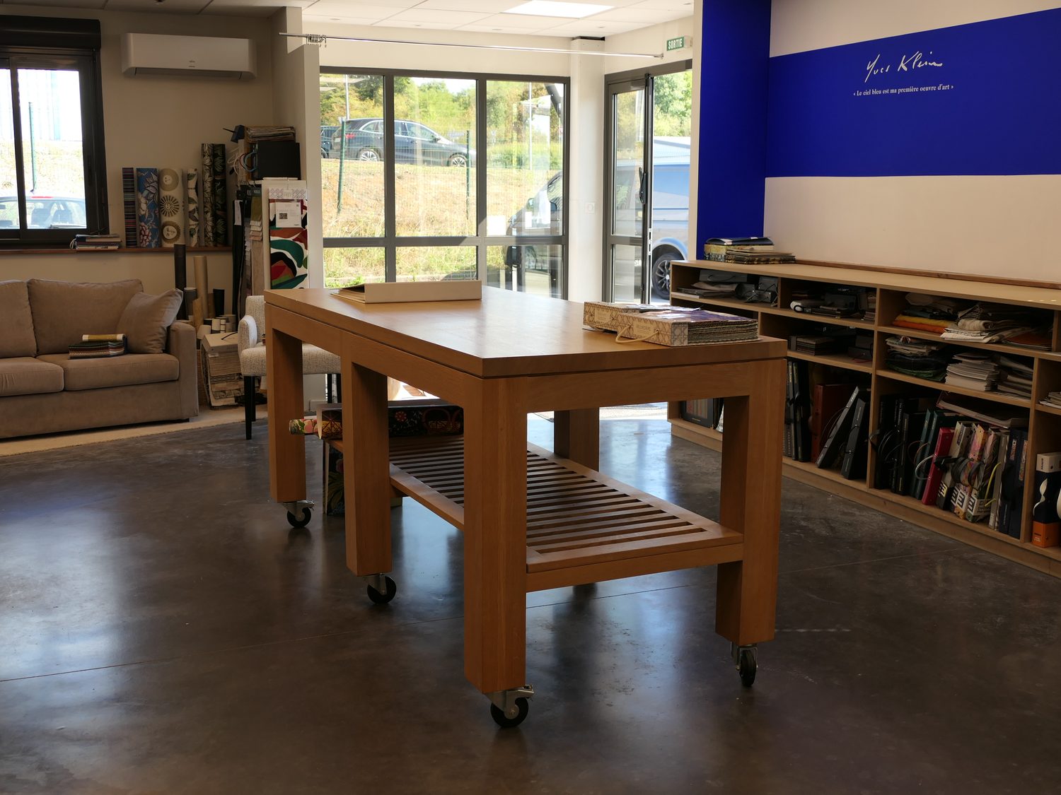 Le showroom : grande table de conseil en bois, bibliothèque de nuanciers et mur bleu au fond